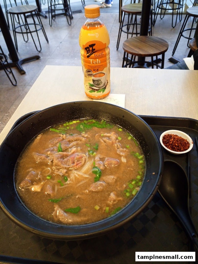 A hearty bowl of beef noodles and a bottle of milk tea on a table at Kaffe Toast.