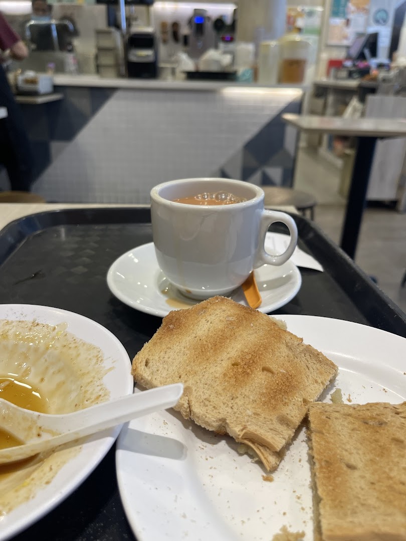 A cup of coffee and toast on a table, with the shop's counter and staff in the background.