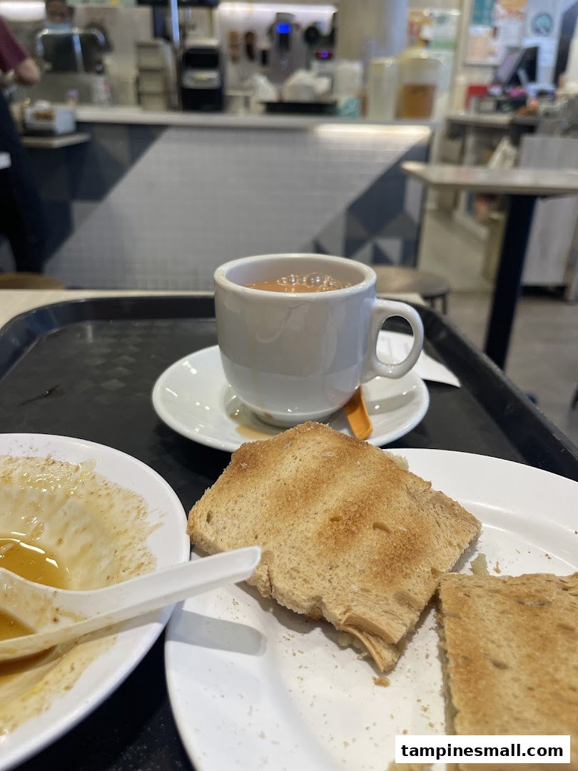 A cup of coffee and toast on a table, with the shop's counter and staff in the background.