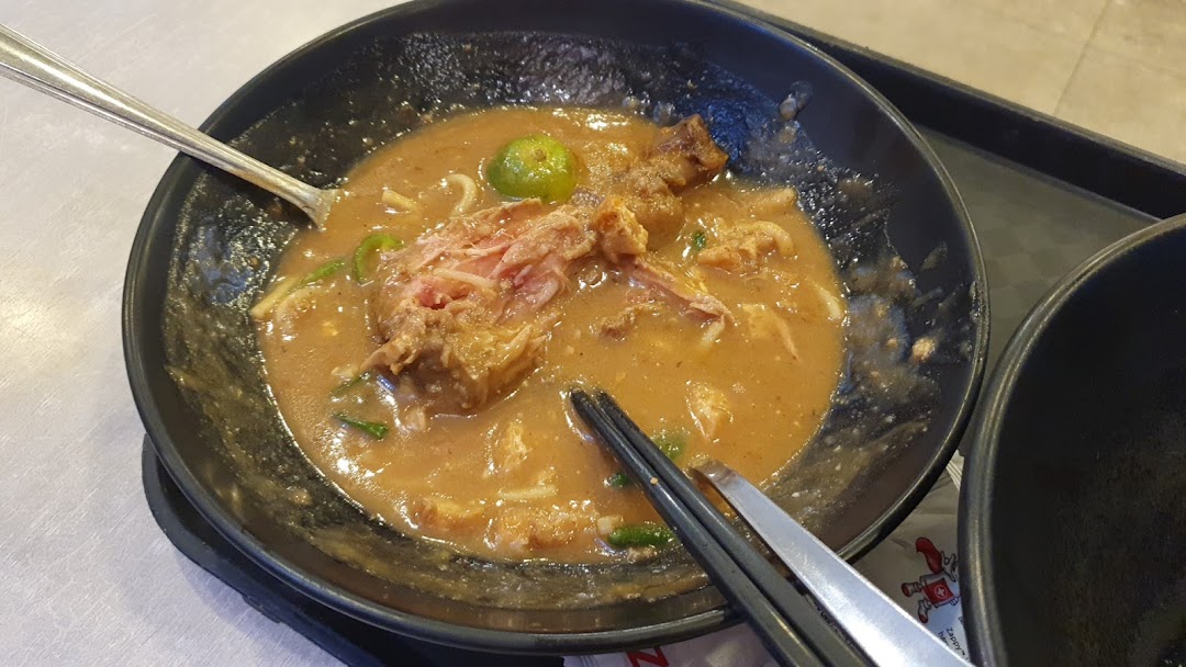 A close-up of a hearty bowl of noodles with meat and gravy, served with a lime.