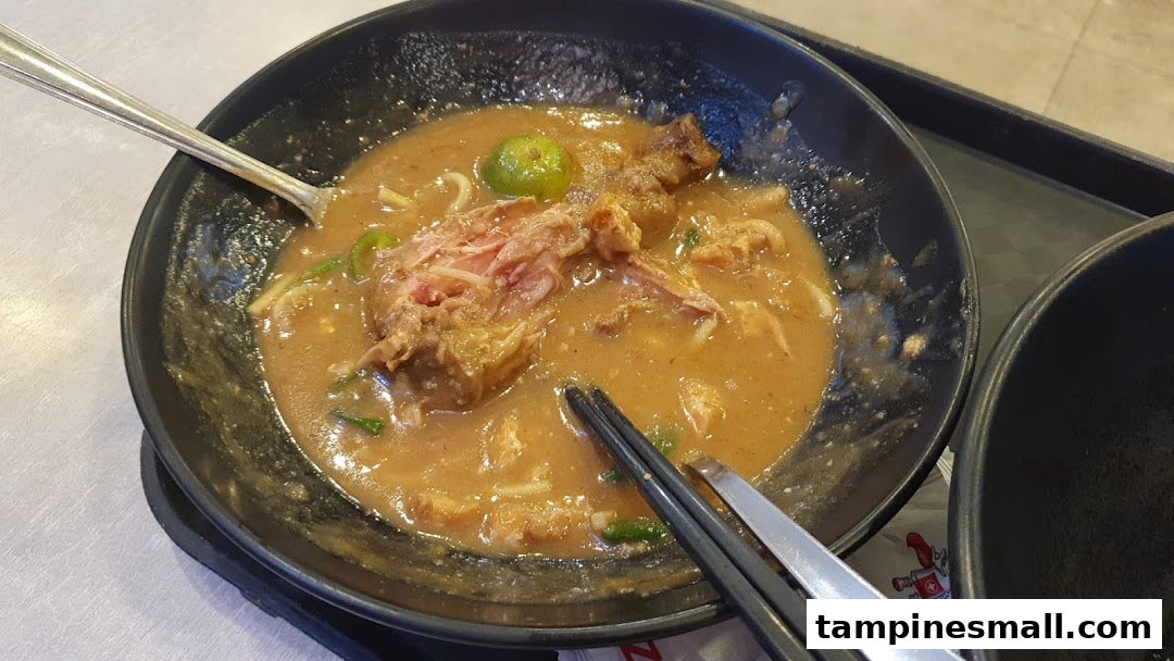 A close-up of a hearty bowl of noodles with meat and gravy, served with a lime.