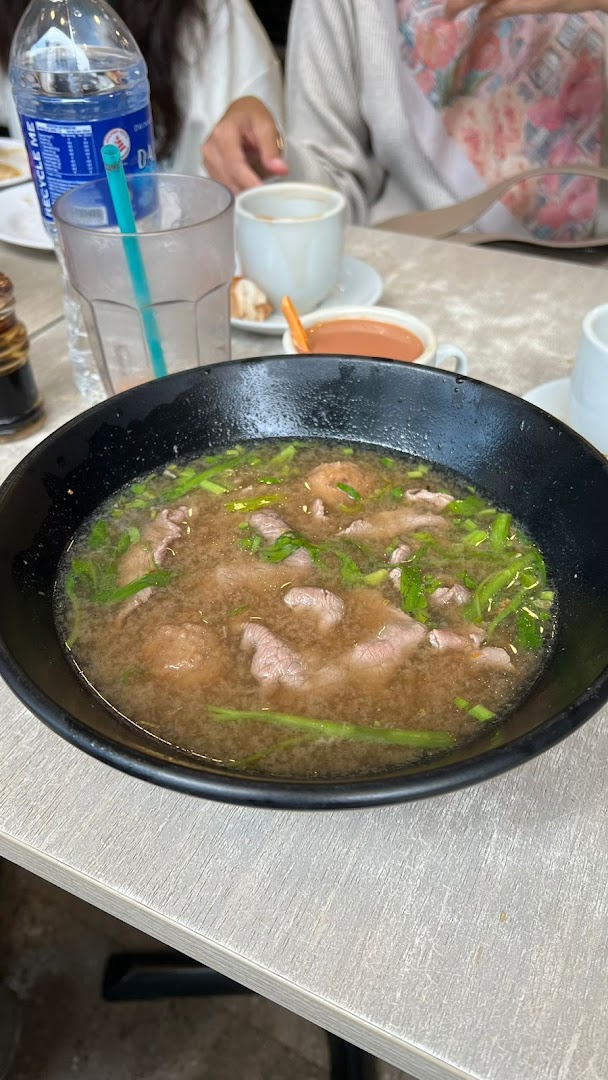 A close-up of a hearty bowl of beef soup noodles with green onions on a table.