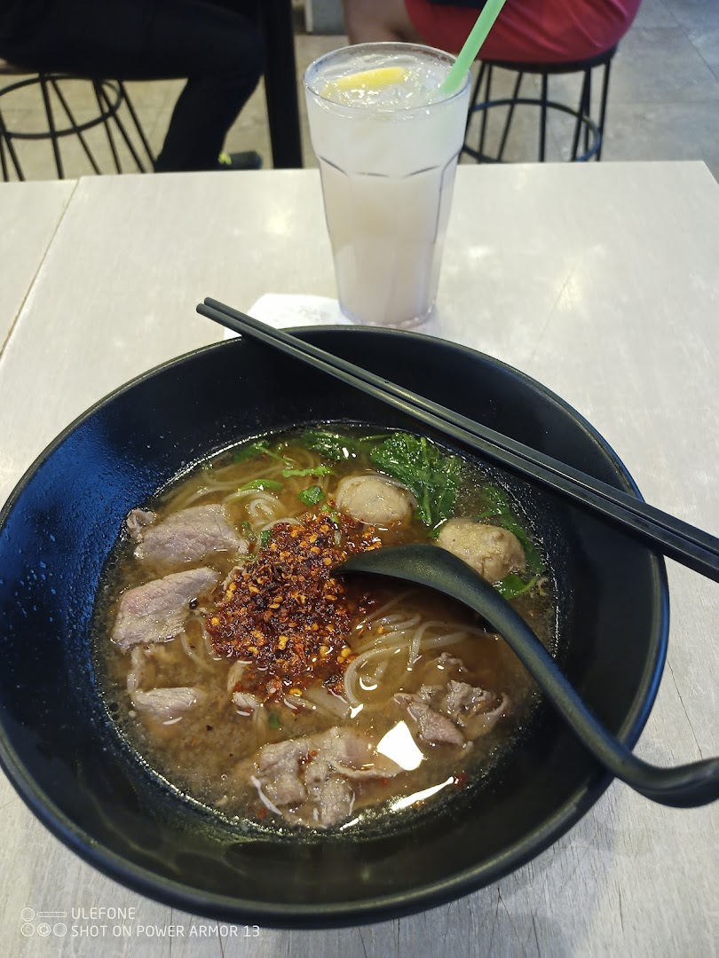 A close-up of a delicious bowl of spicy noodles with beef and a refreshing drink on a table.