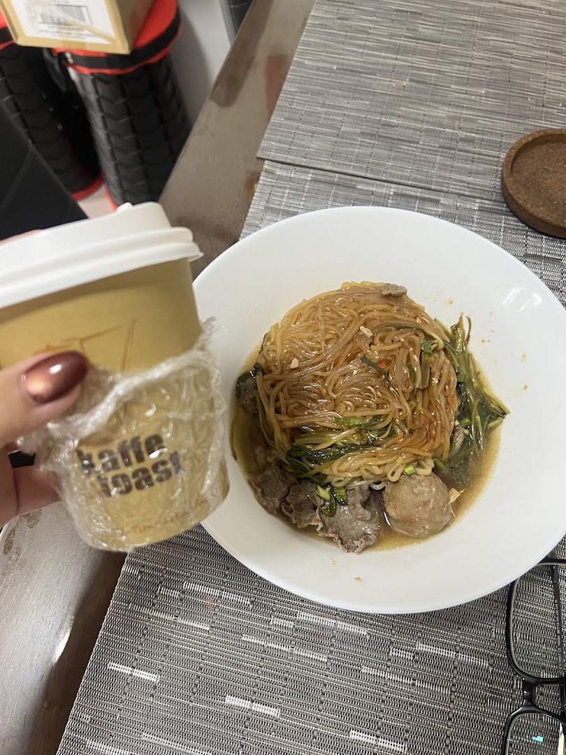 A close-up of a delicious noodle dish with meat and a Kaffe Toast coffee cup.