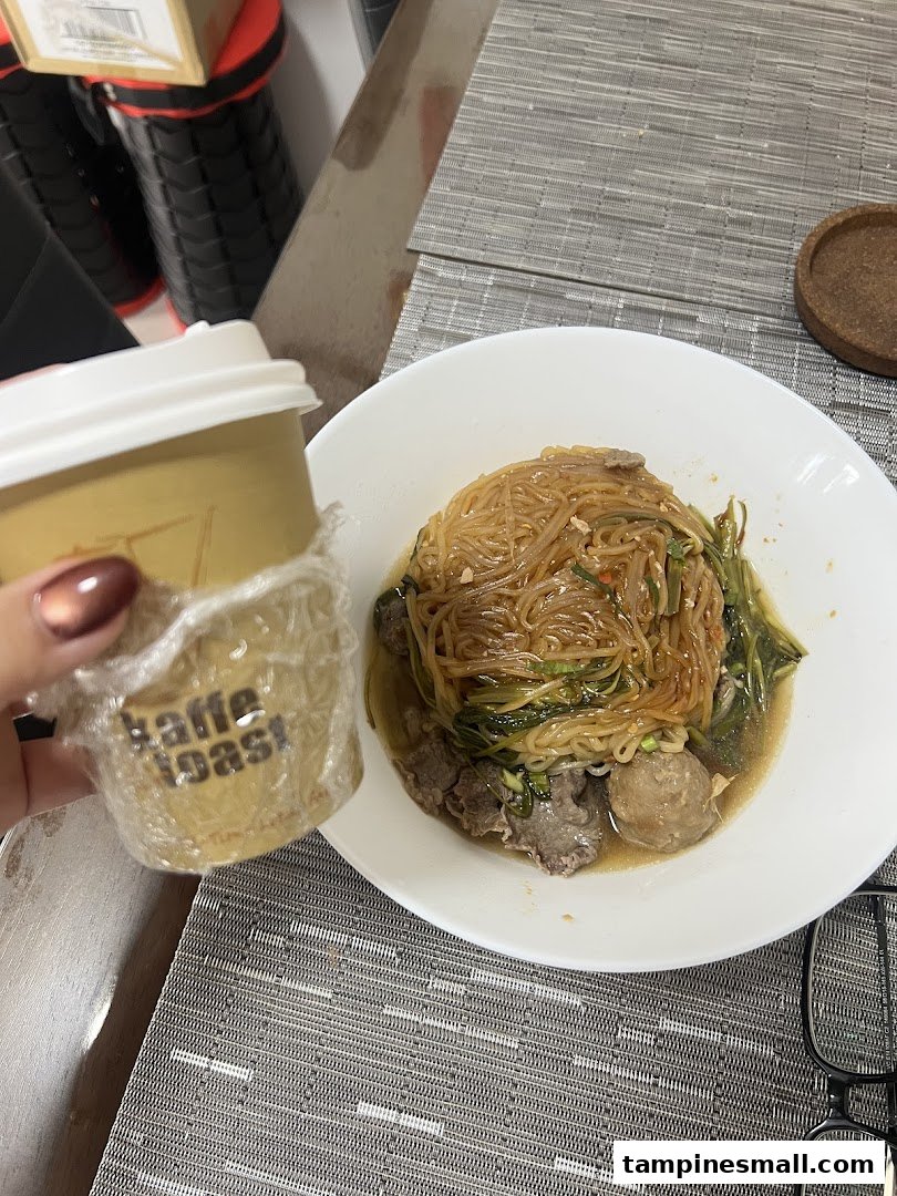 A close-up of a delicious noodle dish with meat and a Kaffe Toast coffee cup.