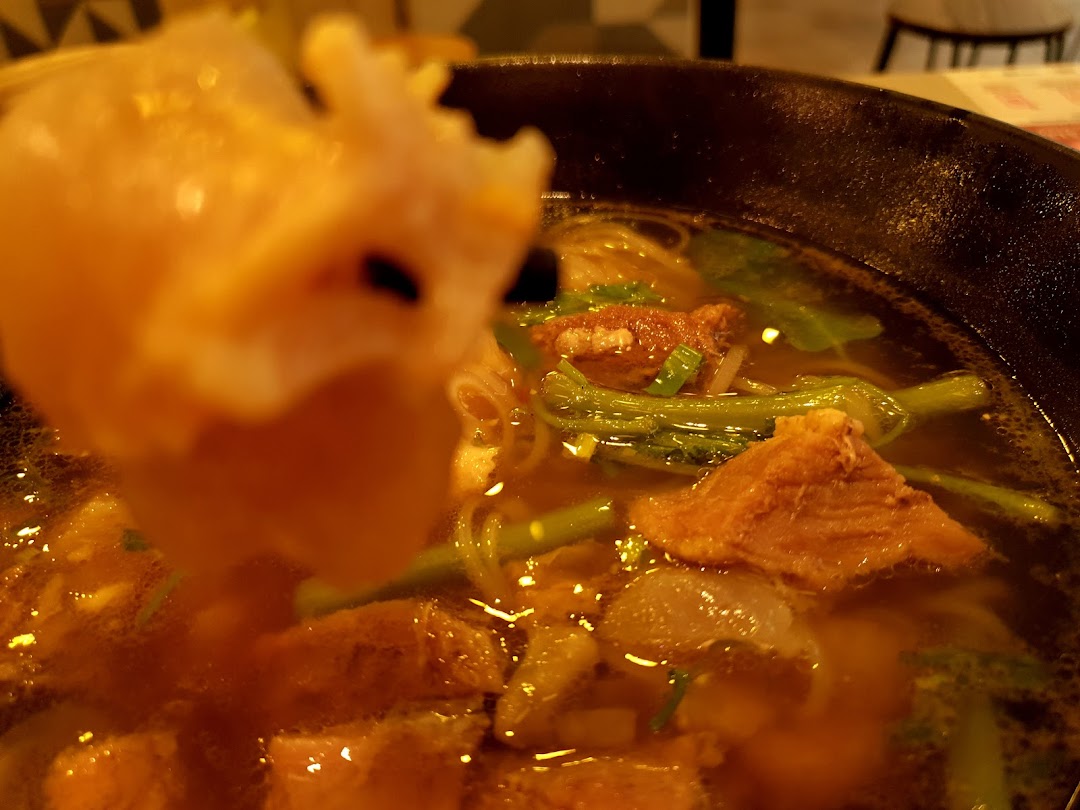 Close-up of a hearty bowl of noodles or soup with tender meat and vegetables, a piece being lifted.