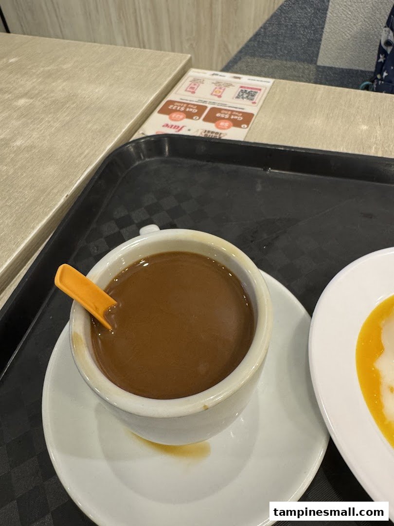 A comforting cup of coffee with an orange spoon and a plate of food on a black tray.