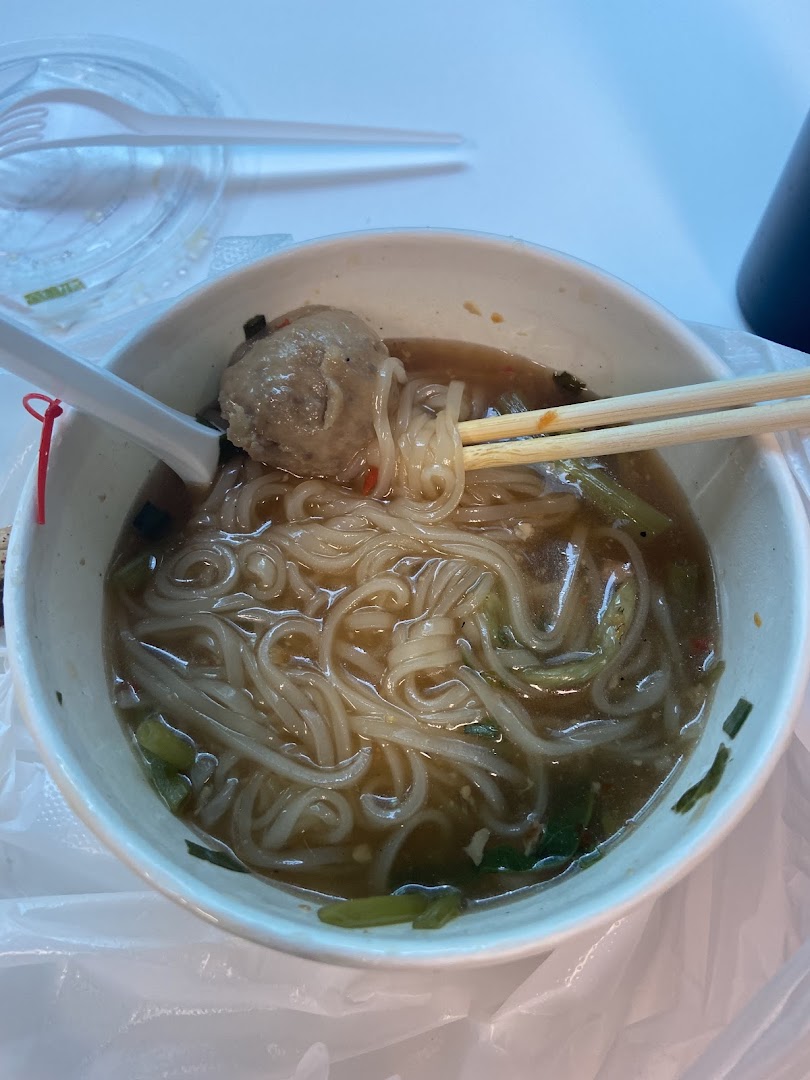 A close-up of a bowl of noodles with a large meatball and chopsticks, ready to be enjoyed.