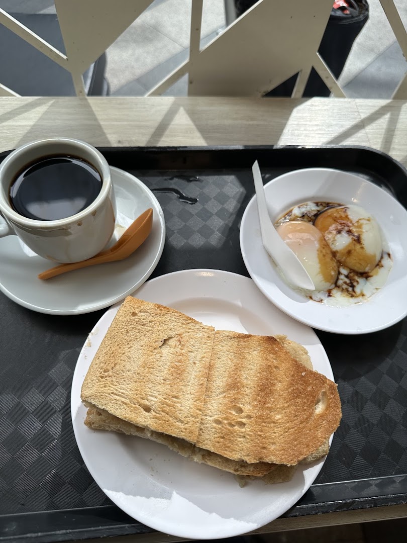 A traditional Singaporean breakfast set featuring coffee, kaya toast, and soft-boiled eggs.