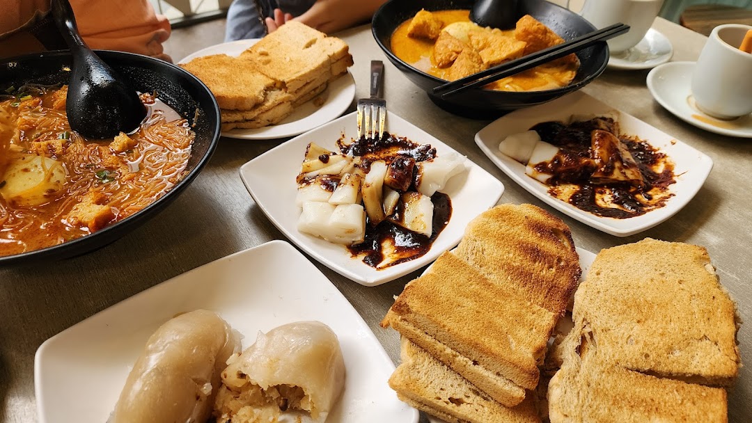 A table filled with various local dishes, including noodles, toast, and rice rolls.