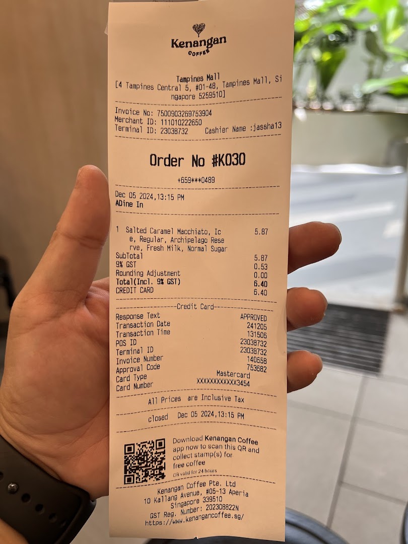 A hand holds a detailed Kenangan Coffee receipt from Tampines Mall, showing a coffee order.