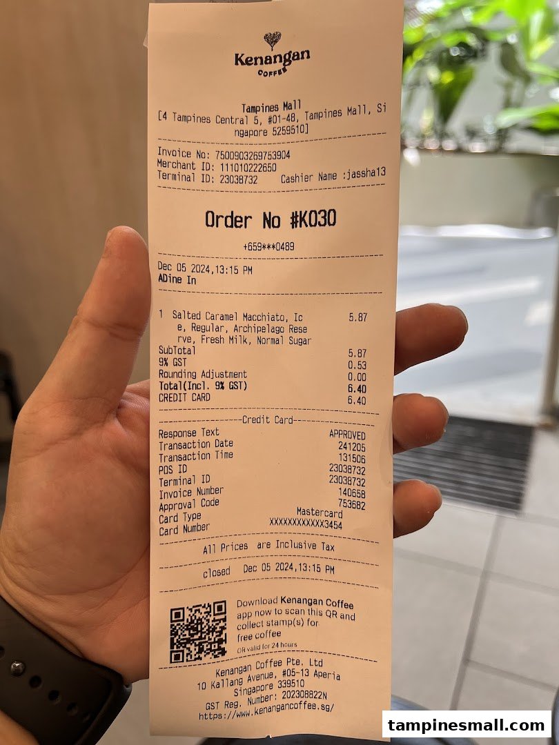A hand holds a detailed Kenangan Coffee receipt from Tampines Mall, showing a coffee order.