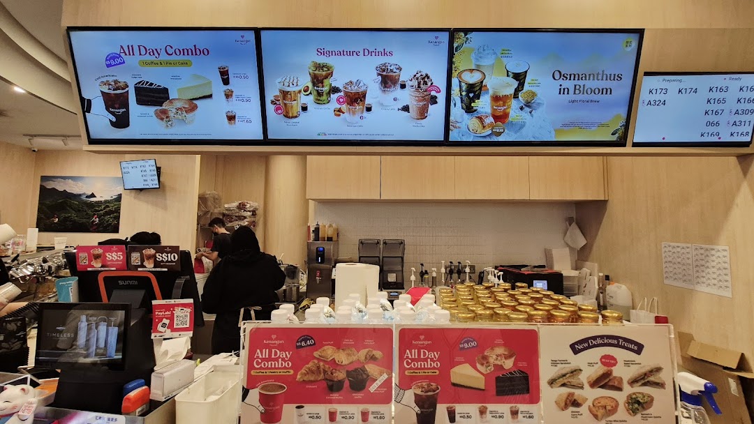 Interior view of Kenangan Coffee's counter, featuring digital menu boards, physical displays, and staff.
