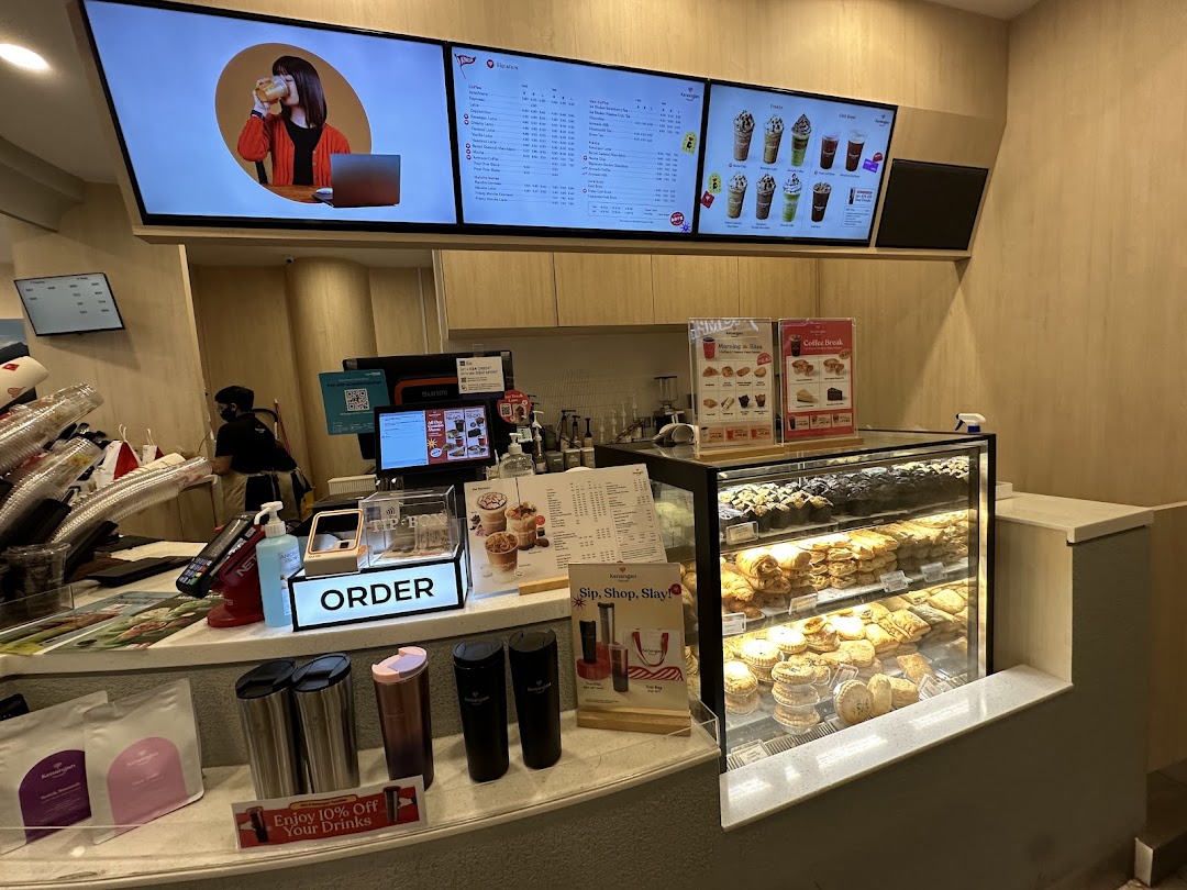 Interior view of Kenangan Coffee, showing the counter, digital menu boards, and a pastry display.