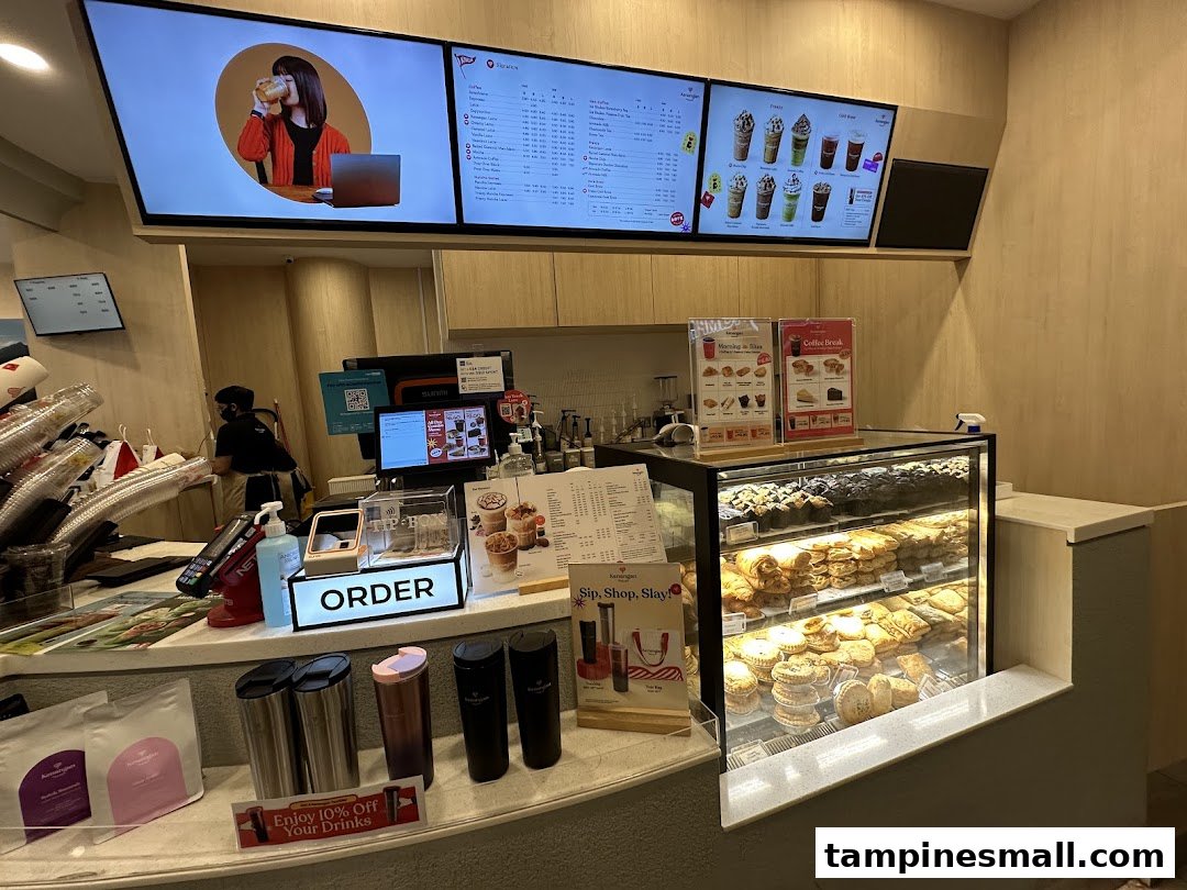 Interior view of Kenangan Coffee, showing the counter, digital menu boards, and a pastry display.