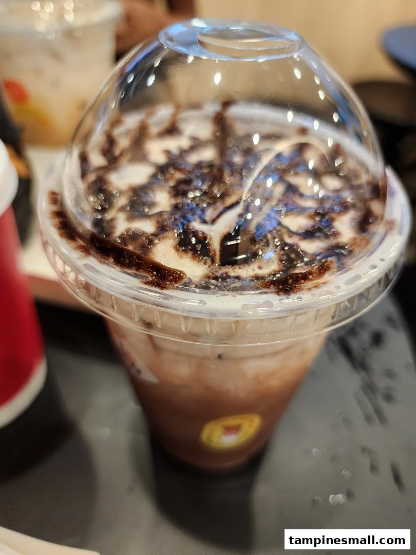 A close-up of a chocolate-drizzled iced coffee drink with a clear dome lid from Kenangan Coffee.