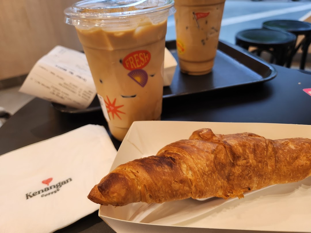 Two iced coffees and a croissant on a table at Kenangan Coffee, perfect for a quick bite.