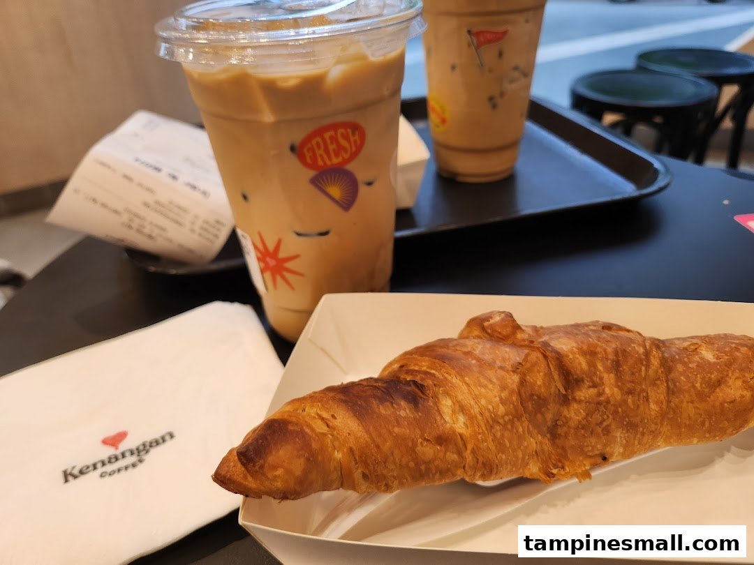 Two iced coffees and a croissant on a table at Kenangan Coffee, perfect for a quick bite.