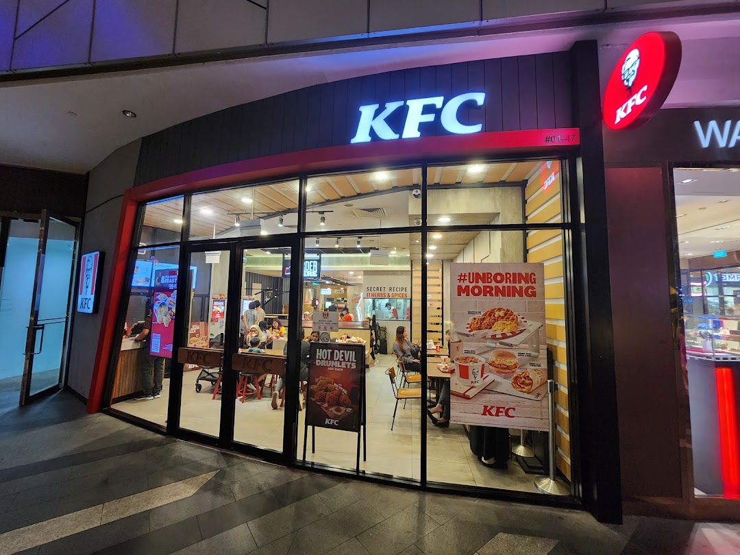 Exterior view of a KFC restaurant with its illuminated logo and glass facade, showcasing the entrance.