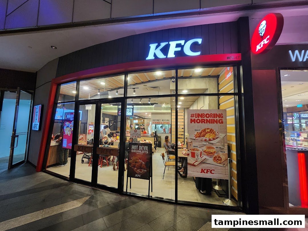 Exterior view of a KFC restaurant with its illuminated logo and glass facade, showcasing the entrance.