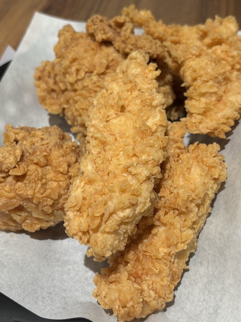 Close-up of several golden-brown, crispy fried chicken tenders or strips on white paper.