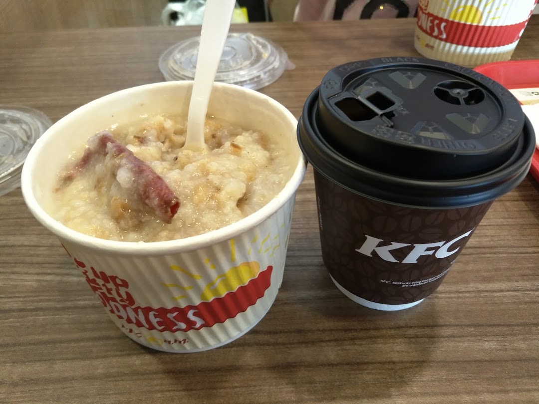 A bowl of congee/porridge with meat and a KFC branded coffee cup on a wooden table.