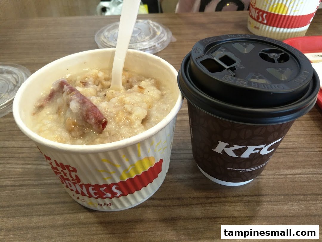 A bowl of congee/porridge with meat and a KFC branded coffee cup on a wooden table.