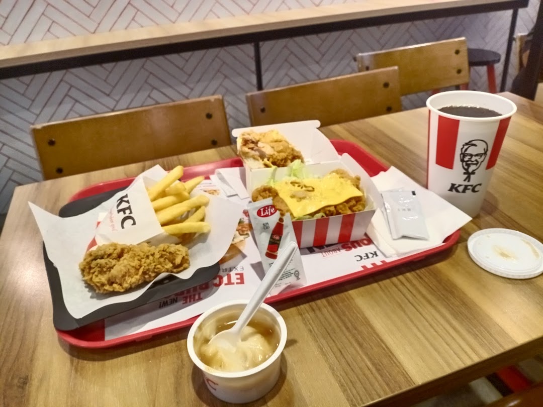 A tray with KFC fried chicken, fries, a chicken burger, mashed potatoes, and a drink on a wooden table.