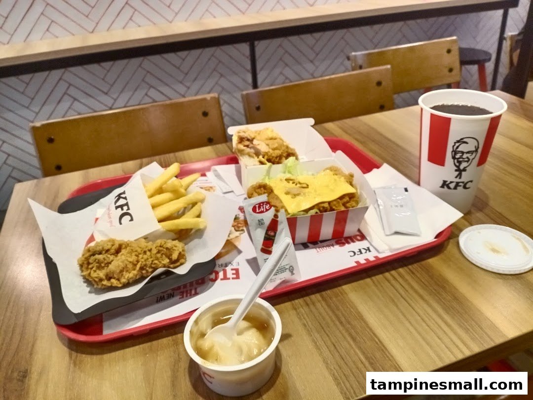 A tray with KFC fried chicken, fries, a chicken burger, mashed potatoes, and a drink on a wooden table.