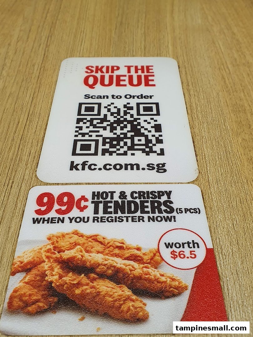 Two KFC promotional cards on a wooden surface, featuring a QR code for ordering and a chicken tenders offer.
