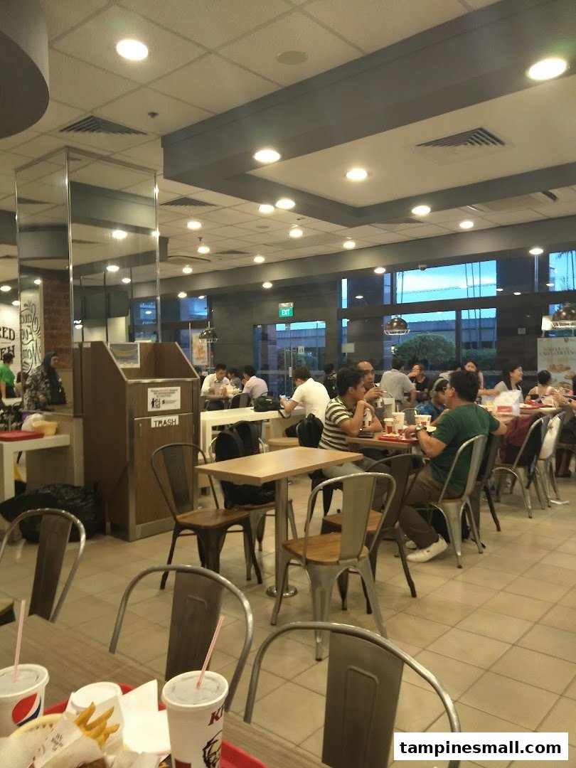 Customers enjoy meals inside a bustling KFC restaurant with modern interior design.