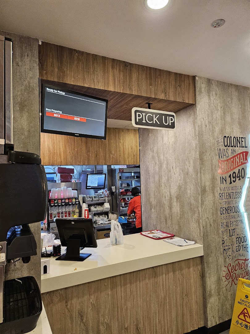 Interior view of KFC's pickup counter with a digital order screen and visible kitchen area.
