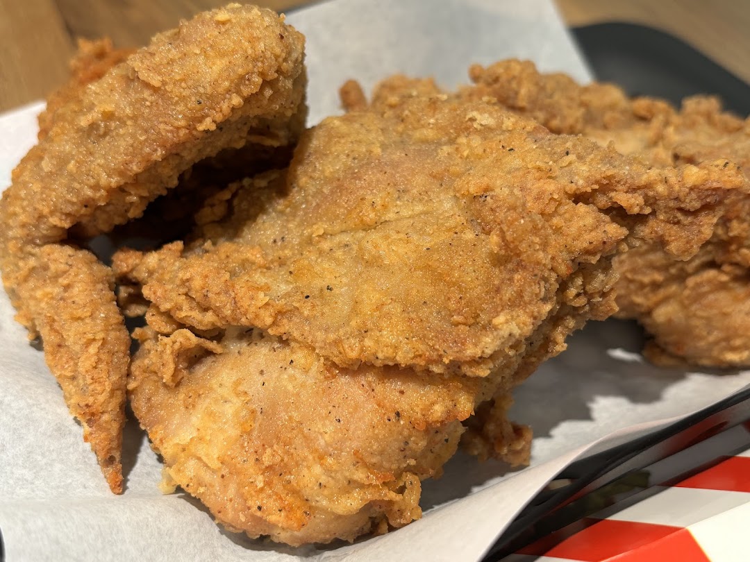 Close-up of crispy, golden-brown fried chicken pieces from KFC, served on white paper.