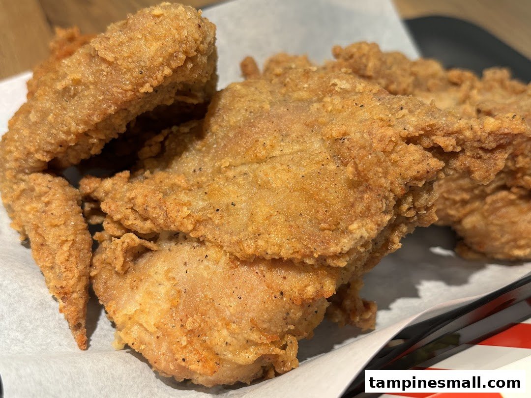 Close-up of crispy, golden-brown fried chicken pieces from KFC, served on white paper.