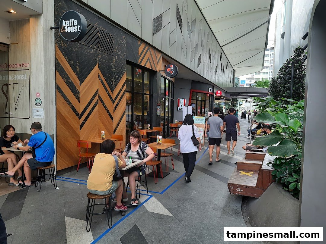 Exterior view of a bustling mall walkway featuring KFC and Kaffe & Toast with outdoor seating.