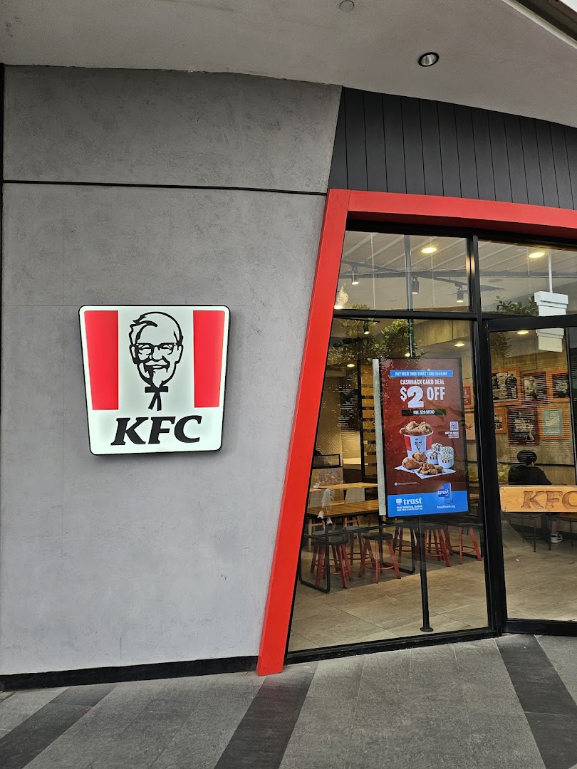 The exterior of a KFC restaurant featuring its iconic logo and a glimpse into the dining area.