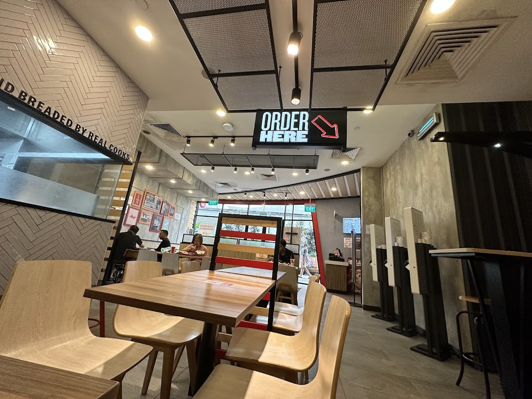 Interior view of a KFC restaurant showing dining area, self-order kiosks, and customers.