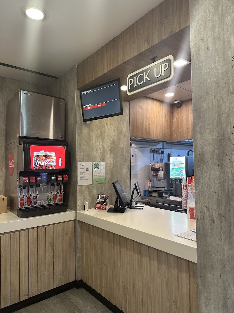 Interior view of KFC's order pickup counter with a soda fountain and digital display.