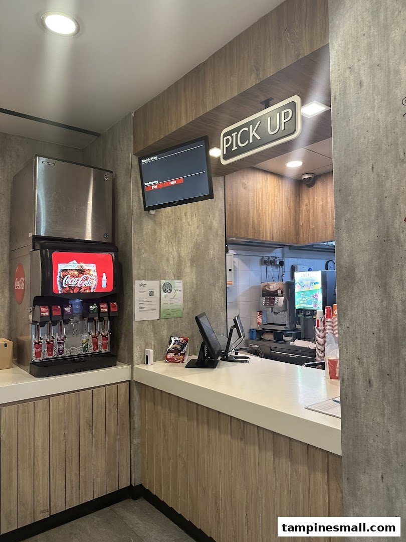Interior view of KFC's order pickup counter with a soda fountain and digital display.