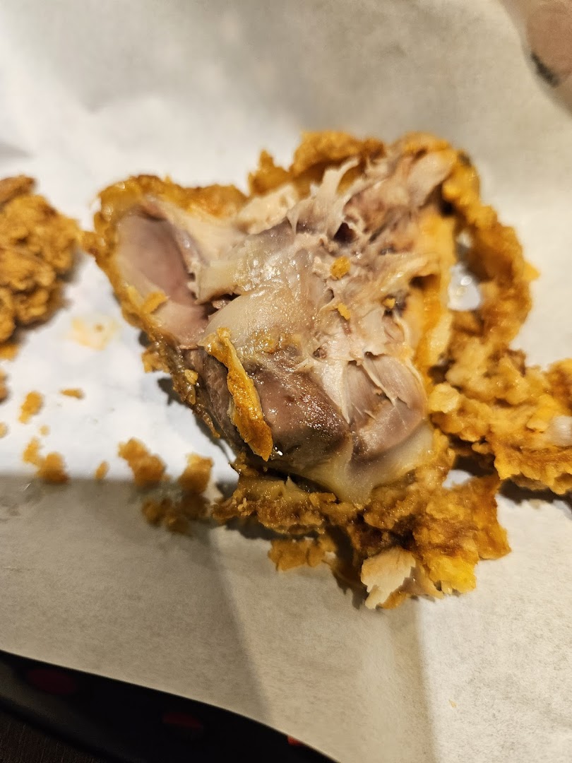 A close-up of a partially eaten piece of crispy fried chicken on white paper.