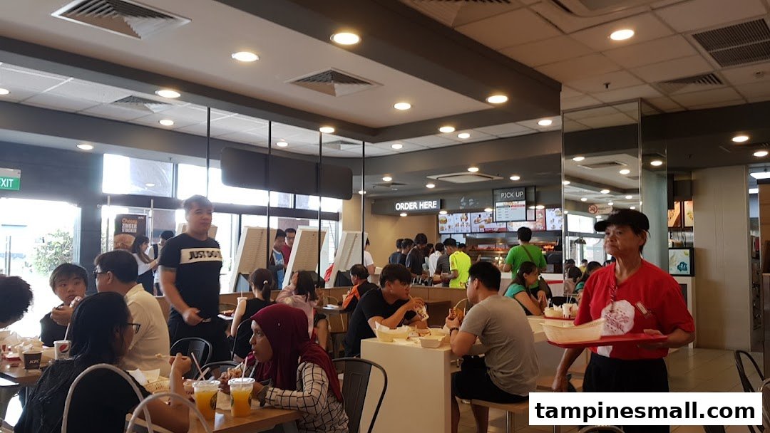 A bustling KFC restaurant interior with customers dining and staff serving food.