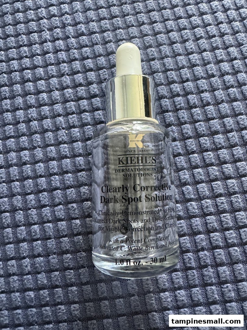 A close-up of Kiehl's Clearly Corrective Dark Spot Solution bottle on a textured surface.