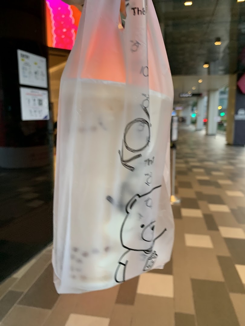 A KOI Thé bubble tea drink in a branded plastic bag, held outdoors.