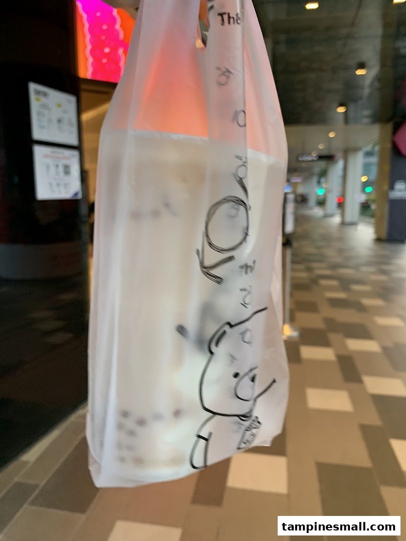 A KOI Thé bubble tea drink in a branded plastic bag, held outdoors.