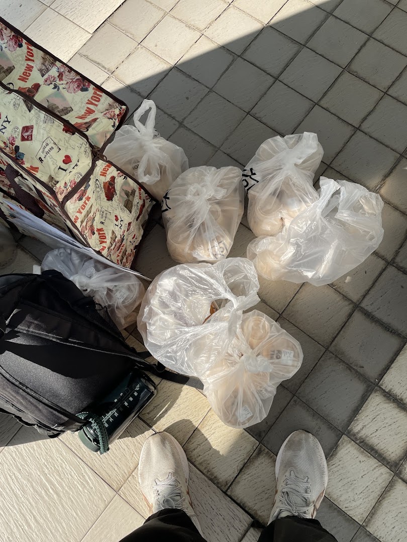 A person's feet, backpack, and multiple plastic bags of purchases on a tiled floor.