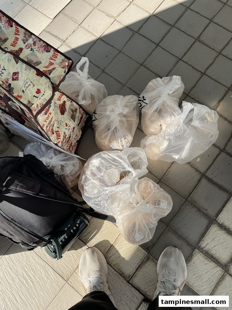 A person's feet, backpack, and multiple plastic bags of purchases on a tiled floor.