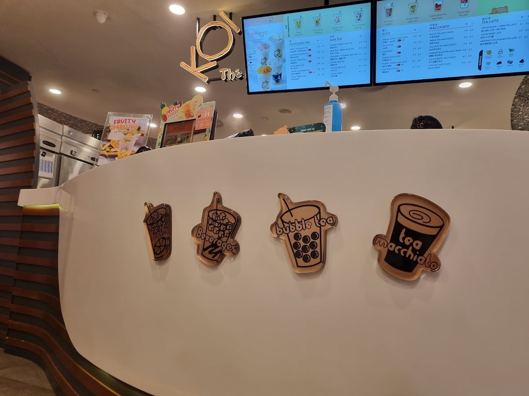 A bright interior shot of KOI Thé's counter with digital menu boards displaying various bubble tea options.