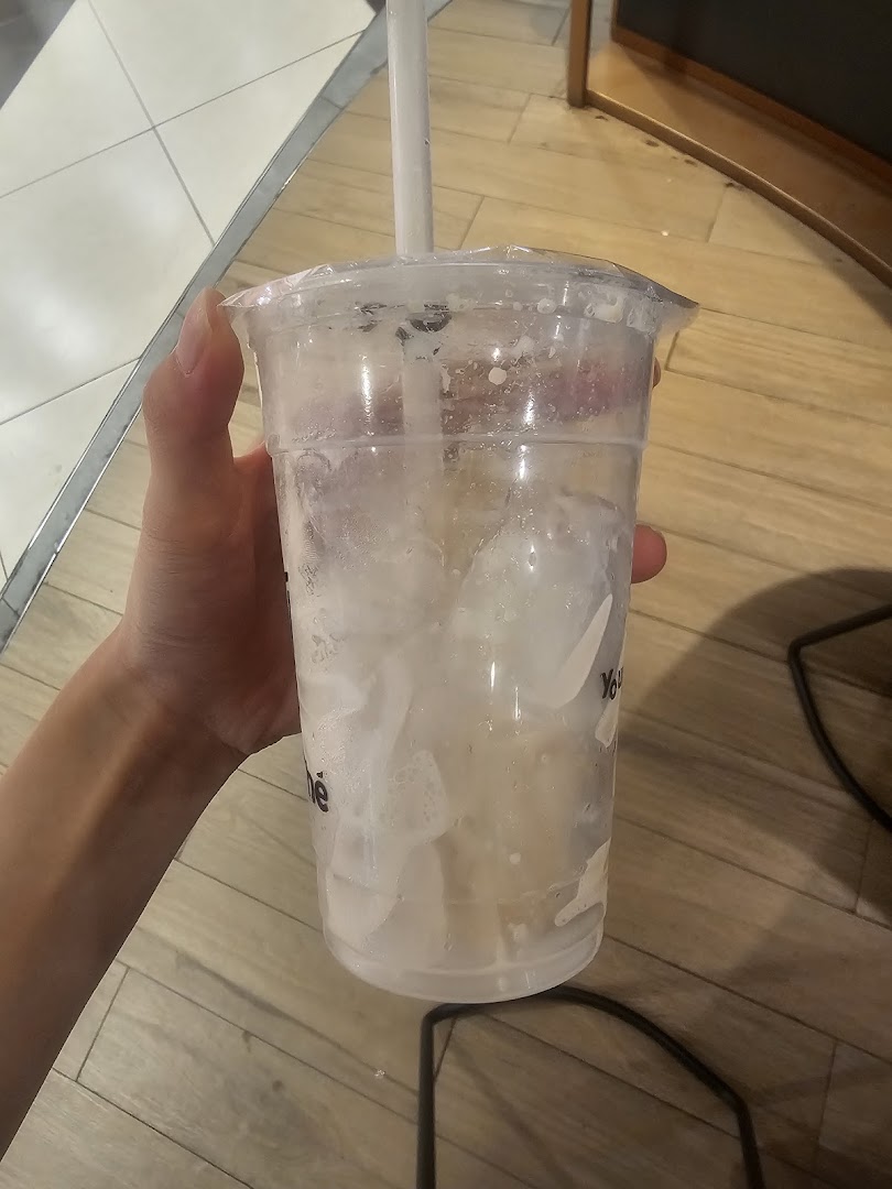 A hand holds a nearly empty KOI Thé bubble tea cup with ice and drink residue.