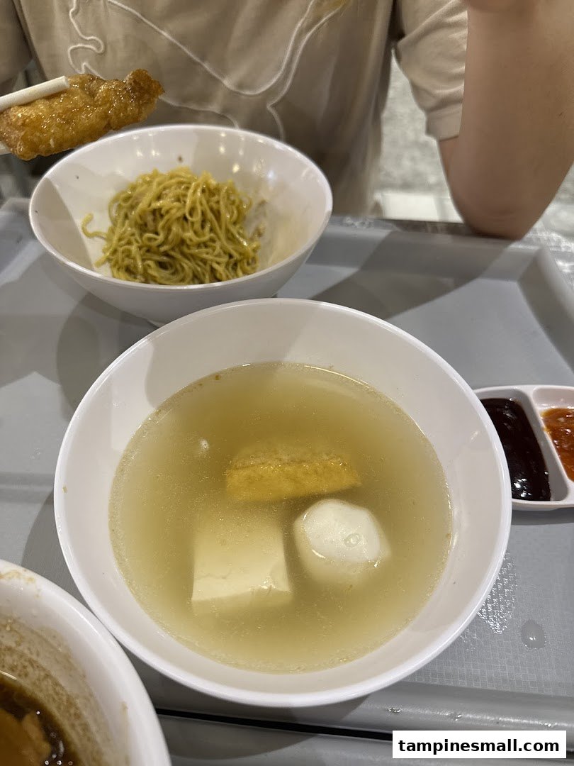 A close-up of delicious Yong Tow Foo soup with various ingredients and a side of noodles.