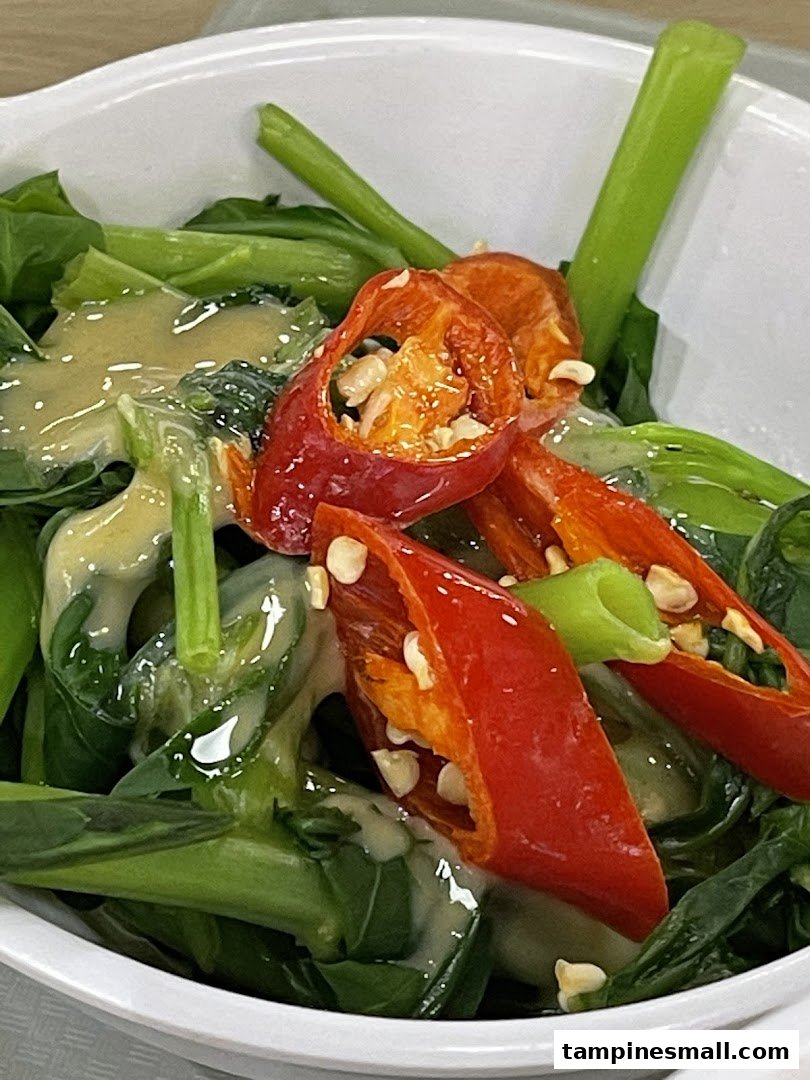 A close-up of vibrant green vegetables topped with sliced red chilies and a creamy sauce.
